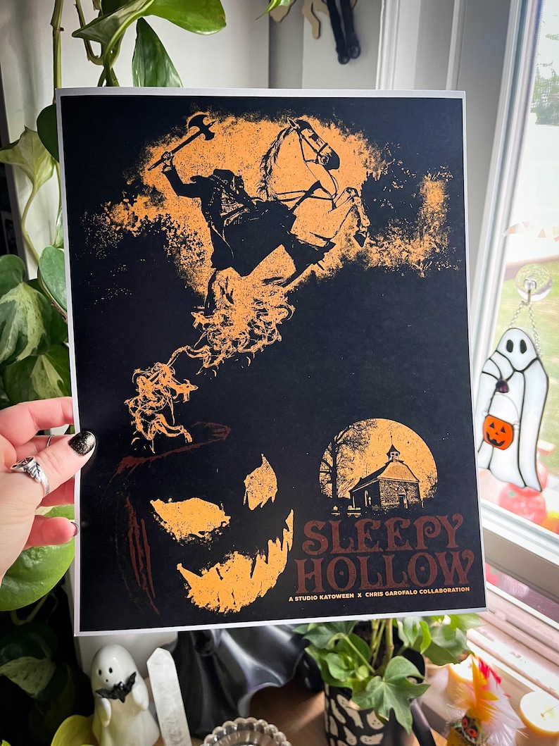 Peut inclure: Une impression noire et orange du Cavalier sans t&ecirc;te chevauchant un cheval avec une citrouille au premier plan. Le texte "Sleepy Hollow" est en bas au centre de l'impression. Une collaboration Studio Katooween x Chris Garofalo.