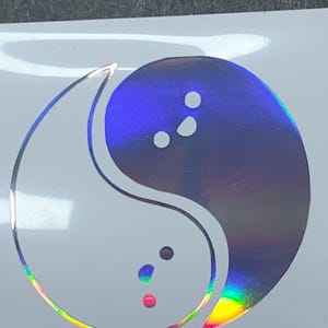 May include: A holographic yin yang symbol with a black and white design. The yin yang symbol is a popular symbol of balance and harmony.