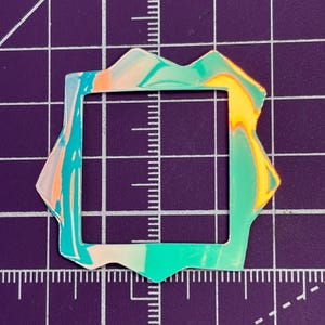 May include: A colorful, abstract square-shaped object with a unique, irregular border. The object features a blend of teal, orange, and yellow hues, creating a marbled effect. The square is set against a purple grid background.