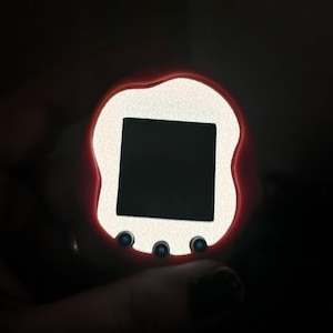 May include: A red and white digital pet toy with a black screen and four blue buttons.