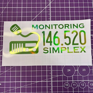 May include: A holographic sticker with the words "MONITORING 146.520 SIMPLEX" in green. The sticker also features a green illustration of a radio and microphone.