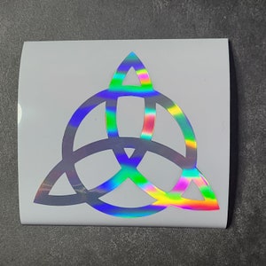 K&ouml;nnte beinhalten: Ein silberner holografischer Vinyl-Aufkleber mit einem Triquetra-Design. Die Triquetra ist ein Symbol f&uuml;r drei miteinander verbundene Kreise, die oft mit Spiritualit&auml;t und der Trinit&auml;t in Verbindung gebracht werden.
