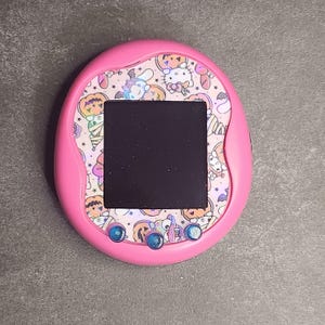 May include: Pink handheld electronic pet toy with a black screen and a Halloween-themed design featuring Hello Kitty and other characters.