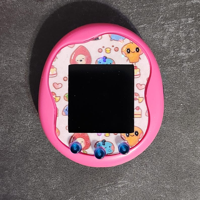 May include: A pink handheld electronic pet toy with a black screen and colorful cartoon characters on the front. The toy has three blue buttons on the bottom.