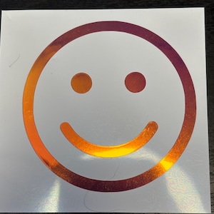 May include: A gold and red smiley face sticker with a white background.
