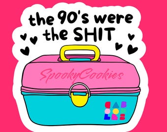 May include: A pink and blue plastic vanity case with a yellow handle and lock. The case has the text "SpookyCookies" written on it. The sticker has the text "the 90's were the SHIT" with hearts around it.