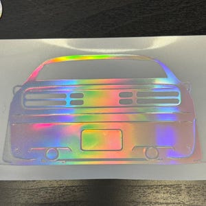 May include: A rear view of a silver car with a holographic finish. The car has a black bumper and a black license plate.