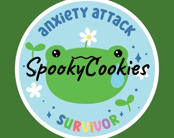 May include: A round sticker with a green frog face, a white daisy, and the words "anxiety attack" and "survivor" in blue and rainbow colors. The sticker also has the text "SpookyCookies" in black.