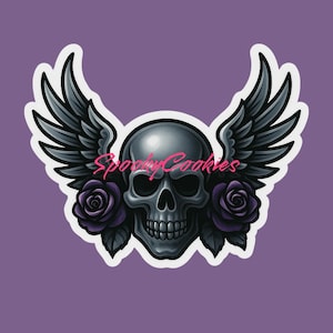 May include: A sticker featuring a detailed skull with feathered wings and two purple roses. The skull is gray with dark shadows, and the wings are black. The text "Spooky Cookies" is written across the skull in pink.
