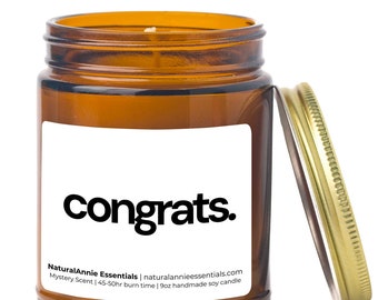 May include: A brown glass candle jar with a white label that says "congrats." The candle is a soy candle with a mystery scent and a burn time of 45-50 hours. The candle is 9 ounces.