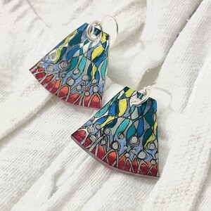 May include: A pair of colorful, abstract earrings with a fan-like shape. The earrings are made of resin and feature a mix of blue, green, yellow, red, and white colors.