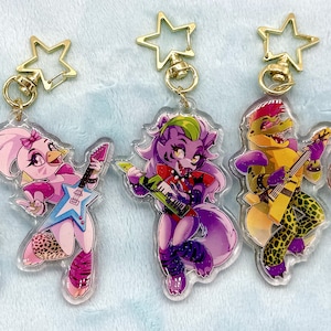 Puede incluir: Cinco llaveros acrílicos transparentes con personajes de dibujos animados tocando la guitarra. Cada llavero tiene un cierre dorado en forma de estrella. Los personajes incluyen un conejo azul, una gallina rosa, un lobo morado, un caimán amarillo y un oso marrón.