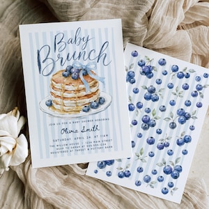 May include: A rectangular invitation card with light blue vertical stripes featuring a watercolor illustration of a stack of pancakes with a blue ribbon and the text Baby Brunch. A second card displays a repeating pattern of blue blueberries.