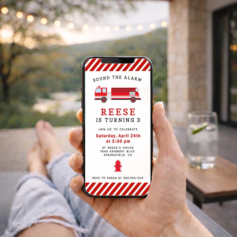 May include: A mobile phone screen shows a birthday invitation with a fire engine design. The text reads "Sound the Alarm, Reese is turning 3." The invitation includes the date, time, and address for the celebration.
