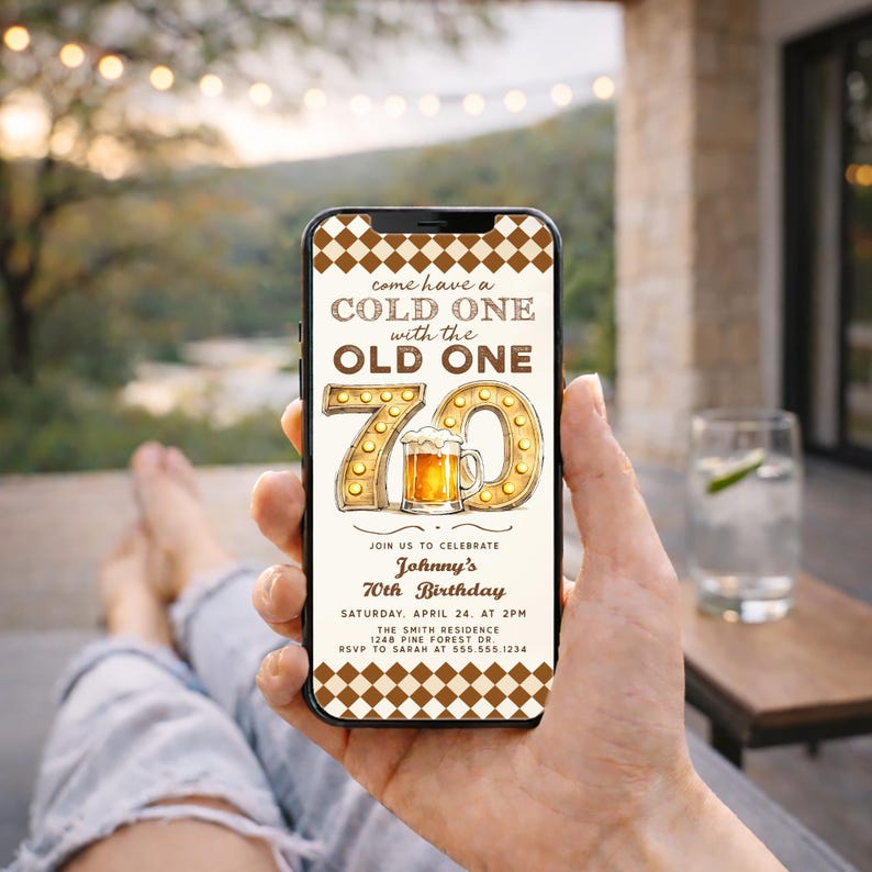 May include: A smartphone displays a birthday invitation with the text "come have a COLD ONE with the OLD ONE." The invitation features a large "70" with a beer mug graphic. The background has a brown checkered pattern.