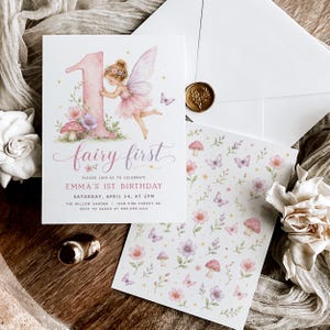 May include: A white birthday invitation card featuring a large pink number one, a watercolor fairy, flowers, and mushrooms. The text reads fairy first, Emma's 1st birthday, Saturday, April 24, at 2pm, The Willow Garden, 1248 Pine Forest Dr, RSVP to Sarah.