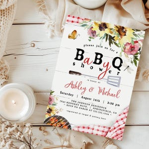 Op de afbeelding: Een uitnodiging voor een BBQ-babyshower met bloemaccenten en de tekst "please join us for a Baby Q shower in honor of Ashley & Michael". De uitnodiging bevat de datum, tijd en locatie.
