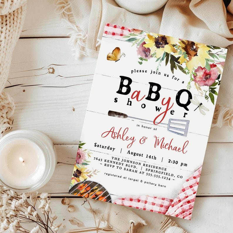Op de afbeelding: Een uitnodiging voor een BBQ-babyshower met bloemaccenten en de tekst "please join us for a Baby Q shower in honor of Ashley & Michael". De uitnodiging bevat de datum, tijd en locatie.