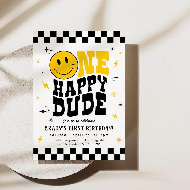 May include: A birthday invitation with a yellow smiley face and the words "ONE HAPPY DUDE" in black and yellow. The invitation includes the text "GRADY'S FIRST BIRTHDAY!" and event details. The design features lightning bolts, stars, and a black and white checkered border.