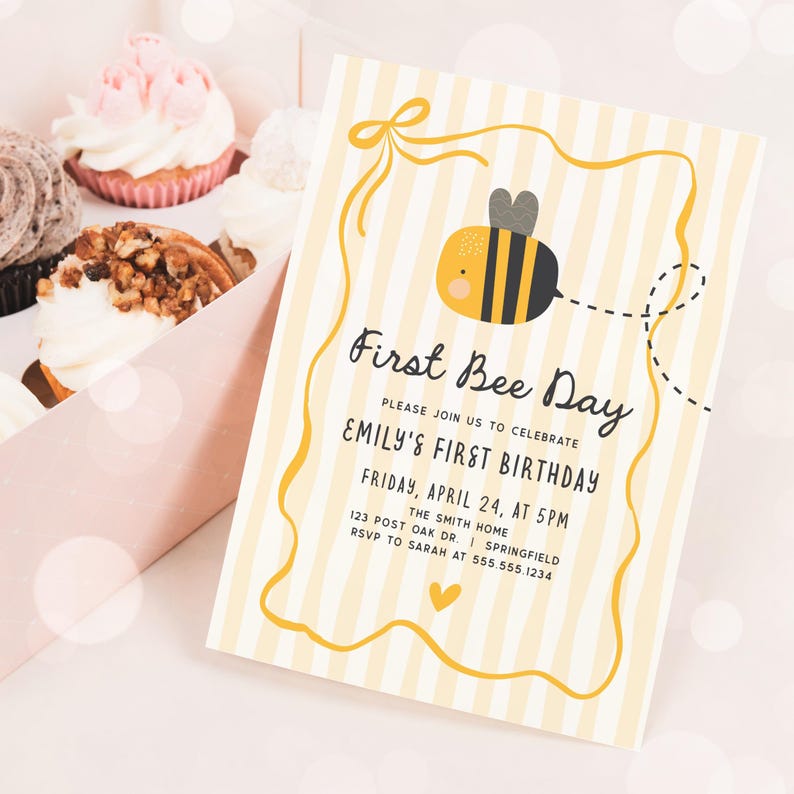 May include: A First Bee Day invitation with a yellow and white striped background. The invitation features a cartoon bee and the text "First Bee Day" with event details. Cupcakes in a pink box are in the background.