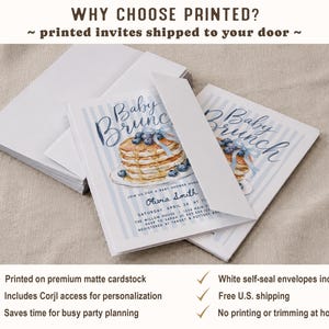 May include: A stack of rectangular baby shower invitations featuring a watercolor illustration of a stack of pancakes with blueberries and a blue ribbon. The text reads Baby Brunch, Olivia Smith, and event details. White envelopes are included with the cards.