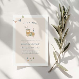 May include: A light peach baby shower invitation with a blue and white banner at the top. The invitation features a cartoon train with a blue smoke plume and the text "IT'S A BOY!" in blue. The text "join us for a baby shower honoring madison williams" is in blue. The text "saturday, april 24, at 2pm" is in blue. The text "past oak caye I 1248 pine forest dr" is in blue. The text "rsvp to sarah at 555 555 1234" is in blue. The text "registered at target & pottery barn" is in blue. The invitation is decorated with small blue, green, and yellow stars.
