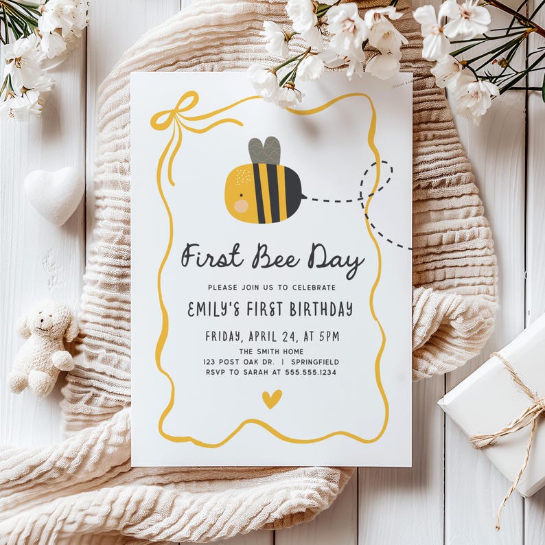 May include: A white invitation card with a yellow border and a cartoon bee illustration. The text reads "First Bee Day" and announces Emily's first birthday on April 24th at 5 PM. The invitation includes RSVP details.
