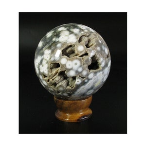 May include: A large, round, gray and white ocean jasper sphere on a wooden stand. The sphere has a unique, natural pattern of white spots and swirls.