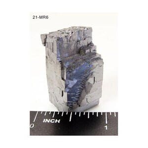 Pu&ograve; includere: Un grande cristallo metallico grigio di forma cubica. Il cristallo &egrave; alto circa 2,5 cm e ha una superficie ruvida e testurizzata. Il cristallo &egrave; etichettato "21-MR6".
