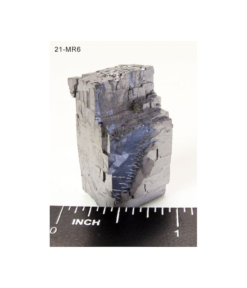 Pu&ograve; includere: Un grande cristallo metallico grigio di forma cubica. Il cristallo &egrave; alto circa 2,5 cm e ha una superficie ruvida e testurizzata. Il cristallo &egrave; etichettato "21-MR6".