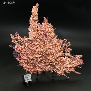 May include: A large, irregularly shaped piece of copper ore with a rough, textured surface. The ore is a reddish-brown color with black accents. A ruler is included for scale, showing the ore is approximately 1 inch in size. Bisbee Minerals is printed on the ruler.