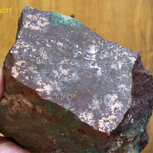 May include: A rough, dark brown rock with a layer of copper on the surface. The copper has a silvery-white sheen and is scattered across the rock. The rock is labeled "22-2CTT".
