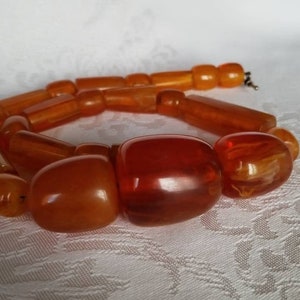 May include: A long amber necklace with large, chunky beads. The beads are a mix of round and rectangular shapes, with a few larger, oval-shaped beads.