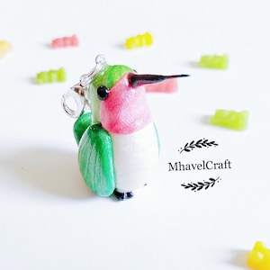 May include: A green, pink and white hummingbird charm with a silver chain. The charm is made of polymer clay and is a handmade piece of jewellery.