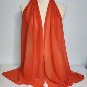 May include: A bright orange chiffon scarf draped over a mannequin. The scarf is lightweight and sheer, with a flowing, drapey texture.