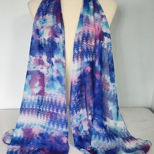 May include: A blue, pink, and white patterned scarf with a matching hair scrunchie. The scarf is made of a sheer fabric and has a flowing design.