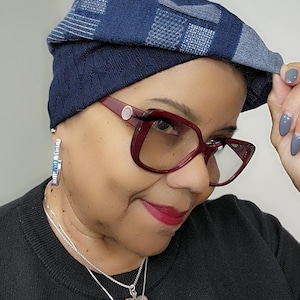 May include: A woman wearing a blue and gray patterned knit beanie, red-rimmed glasses, and a silver necklace with a heart pendant. She is wearing a black sweater.