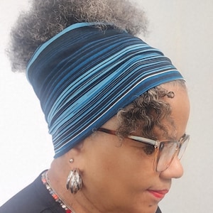 May include: A blue and black striped headband. The headband features horizontal stripes in shades of blue and black. The person is also wearing glasses and silver earrings. The headband is worn on the head.
