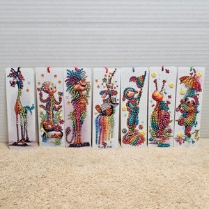 May include: A collection of six rectangular, vertical art pieces featuring whimsical, colorful creatures. Each piece is adorned with small, sparkling embellishments, creating a textured, jewel-like appearance. The creatures include a giraffe, an octopus-like figure, a lion, a bird, a person, and a snail.