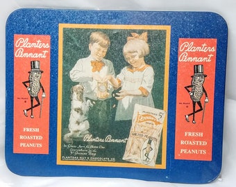May include: A blue and red rectangular tin tray with a vintage advertisement for Planters Pennant Salted Peanuts. The tray features a colorful illustration of two children feeding peanuts to a dog. The text on the tray reads "Planters Pennant" and "Fresh Roasted Peanuts".