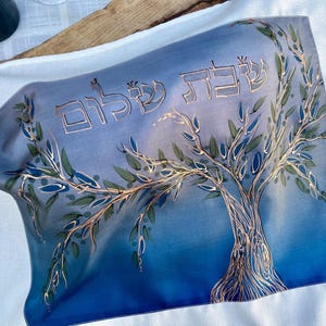 Könnte beinhalten: Ein blauer und weißer Stoff mit einem goldenen Baumdesign und den hebräischen Worten "Shalom" in goldenen Buchstaben.