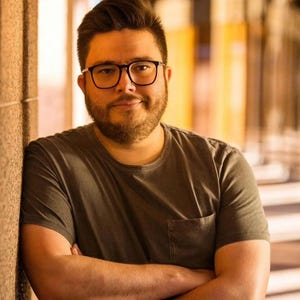 K&ouml;nnte beinhalten: Eine Person mit Brille und einem grauen T-Shirt mit Tasche lehnt an einer Wand. Der Text oben lautet: "Vielen Dank, dass Sie ein treuer Sammler sind!"