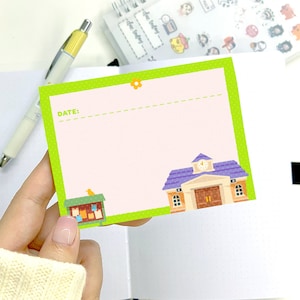 May include: A rectangular sticky note with a light green border and a light pink interior. The note features a schoolhouse illustration and a small birdhouse. The word "DATE:" is printed on the note.