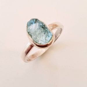 May include: A silver ring with a light blue aquamarine gemstone. The gemstone is a rough, natural shape.