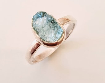 May include: A silver ring with a light blue aquamarine gemstone. The gemstone is a rough, natural shape.