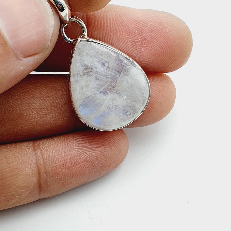 May include: A teardrop-shaped moonstone pendant with a silver bail. The stone is white with a blue iridescent sheen.