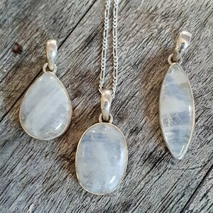 May include: Three silver necklaces with moonstone pendants. The pendants are different shapes: teardrop, oval, and oval with a pointed end.