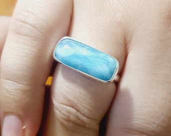 May include: A silver ring featuring a light blue rectangular gemstone. The gemstone has a swirling pattern.