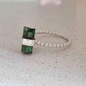 May include: A silver ring with a green tourmaline gemstone. The ring is made of small silver beads.