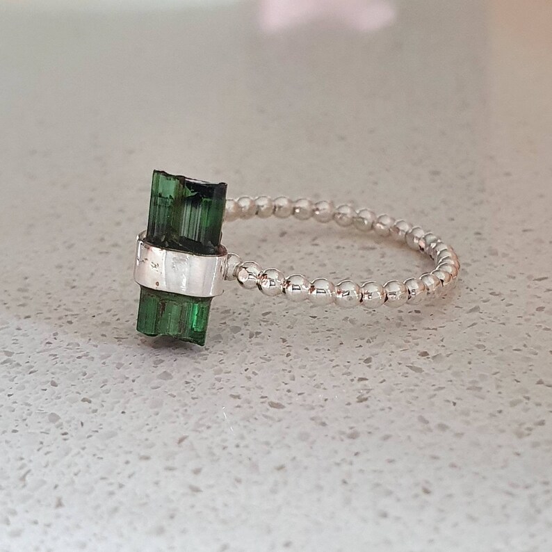 May include: A silver ring with a green tourmaline gemstone. The ring is made of small silver beads.